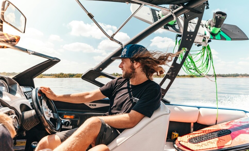 man with his hair blowing in the wind driving a boat